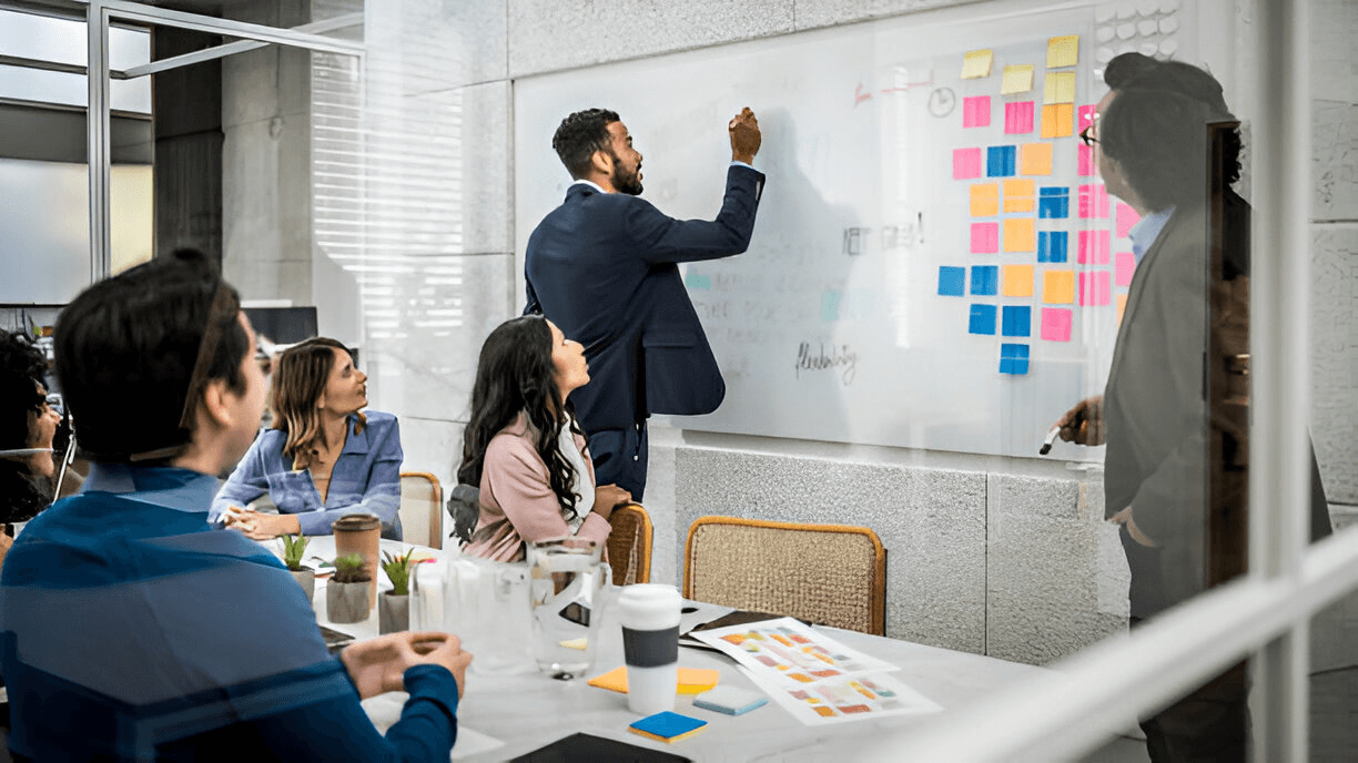 A man writing on a board while addressing his team